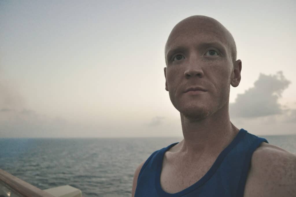 headshot of Chris in a blue tank top and ocean background